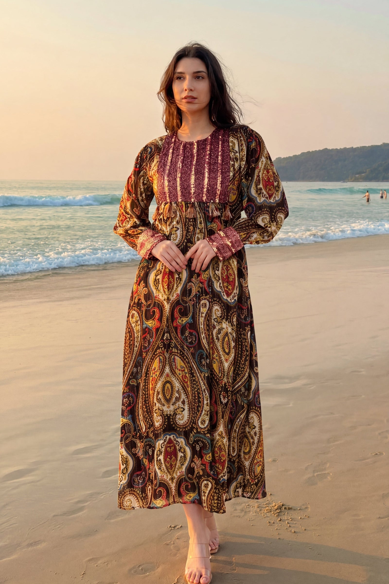 Woman in a patterned dress standing on a beach with ocean and sunset in the background
