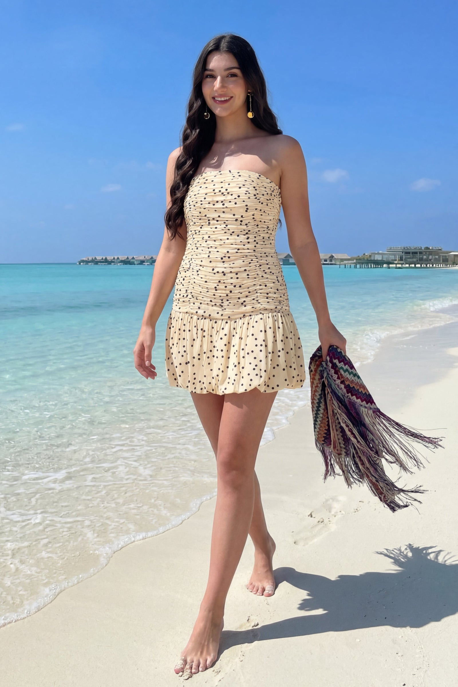 Woman in a yellow dress standing on a beach with clear blue water and sky.