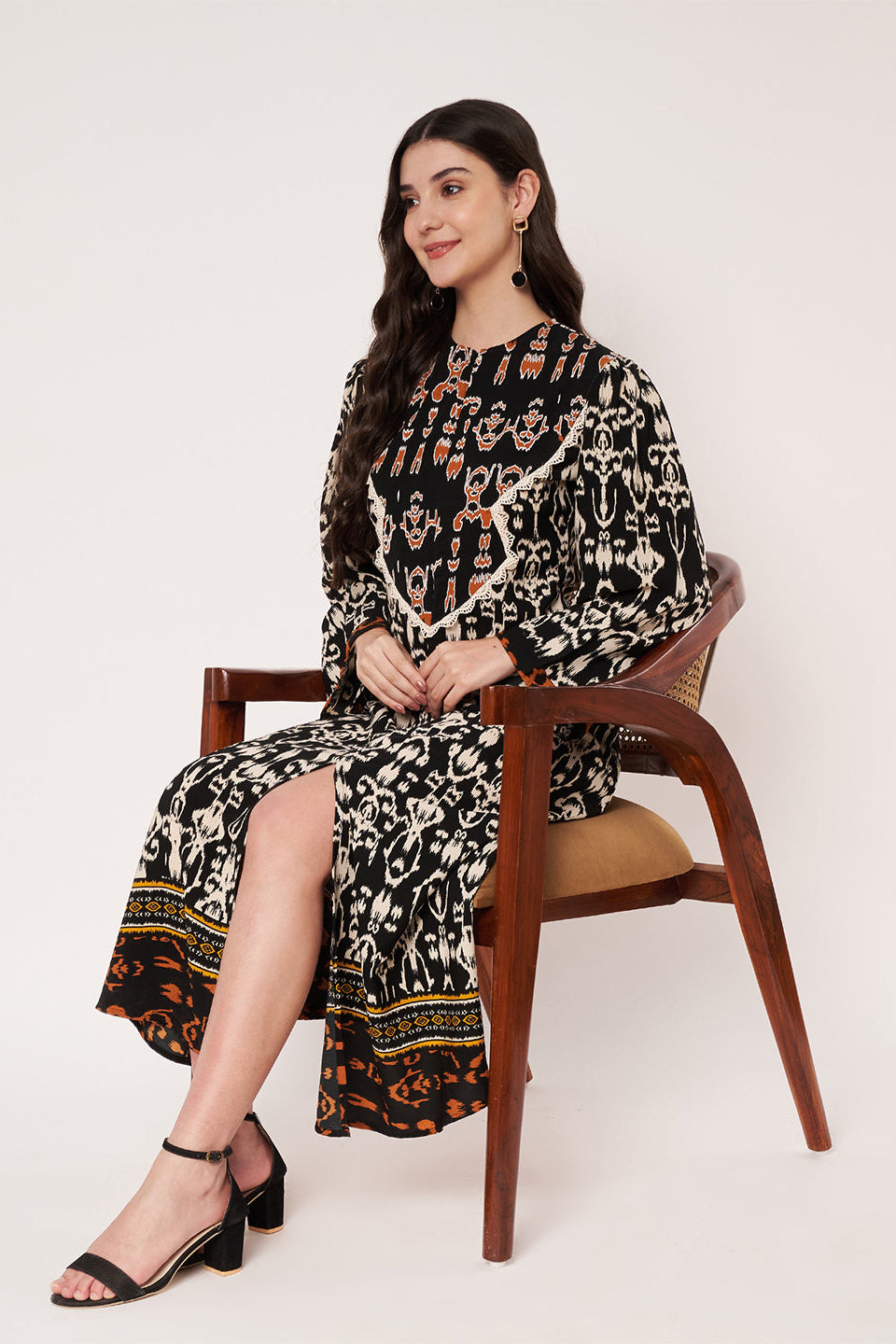 Woman sitting on a chair wearing a patterned dress against a white background